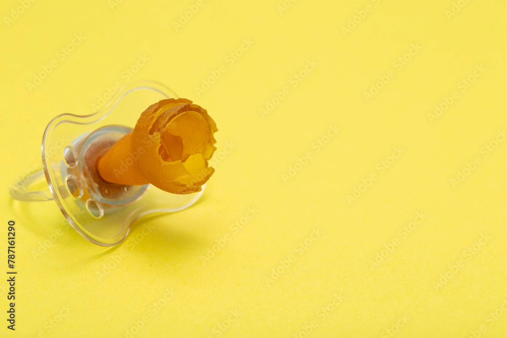 A chewed baby pacifier on a yellow background. Concept of teething in children, close-up. Copy space for text