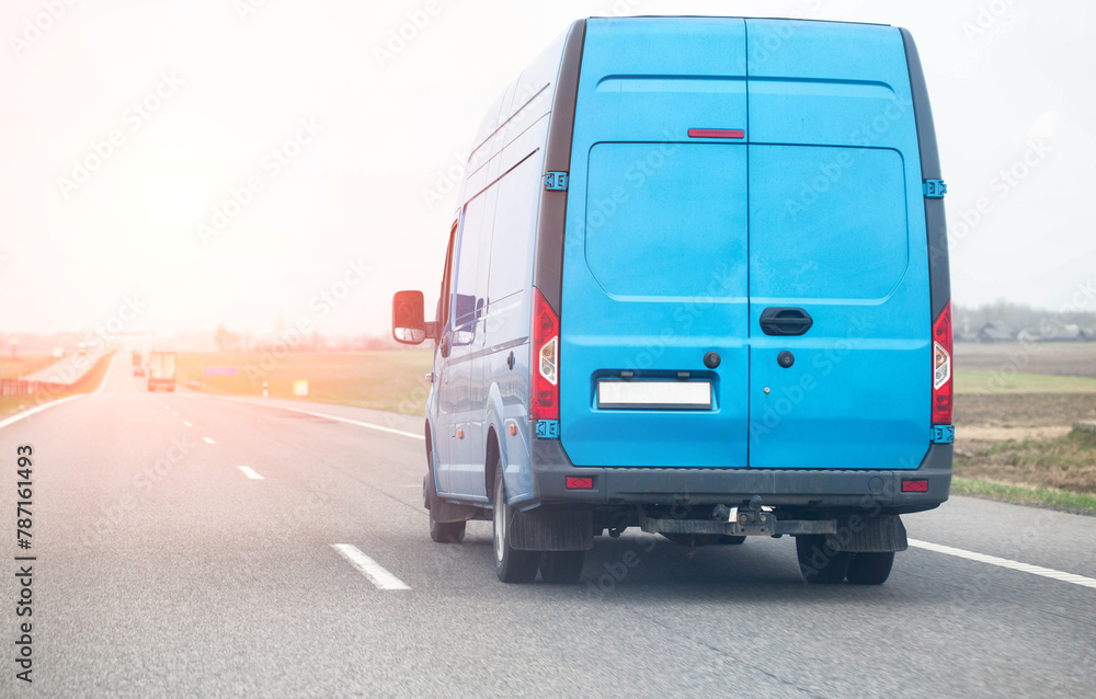 A blue manufactured goods van transports non-food cargo along a highway in the spring against the backdrop of the sun, copy space for text, industry