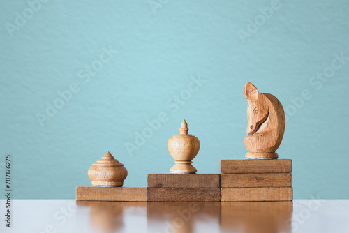 Chess knight on highest wooden block on blurred blue concrete background for winner, winning situation, encounter serious enemy, business competitive, strategy concept photo