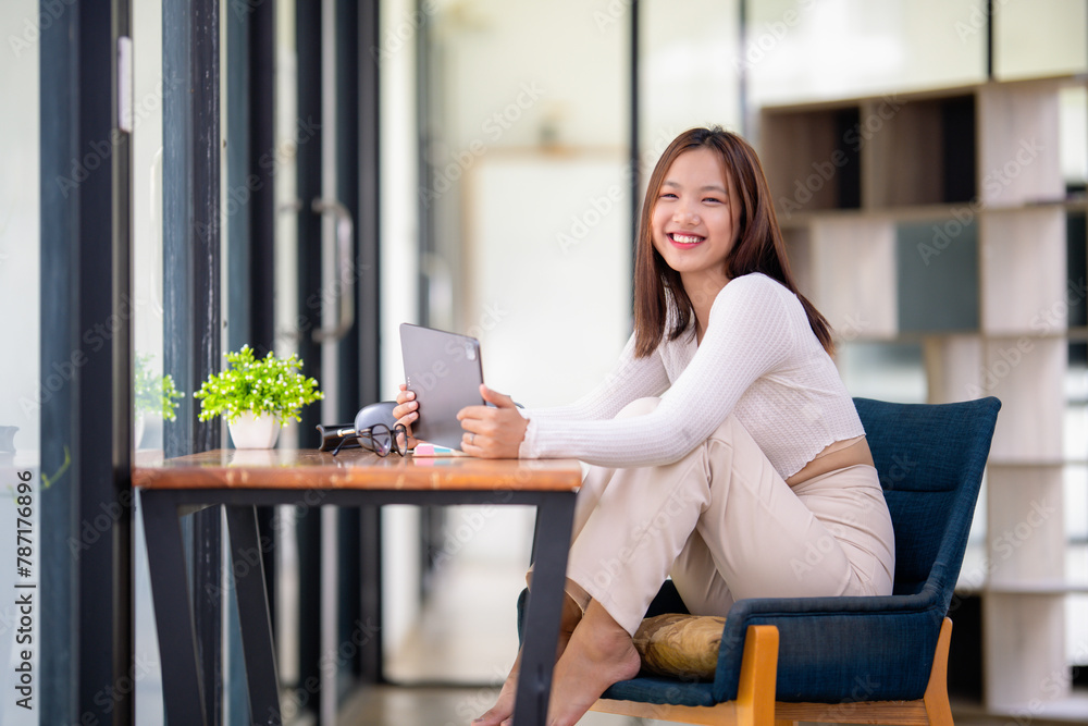 Relaxed young woman smiling as she browses on her tablet, sitting comfortably in a bright modern home.