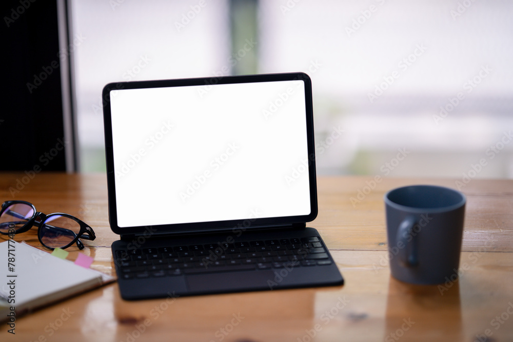 Fototapeta premium Open digital tablet with blank screen. Financial charts, hot coffee, and office supplies are on the table.