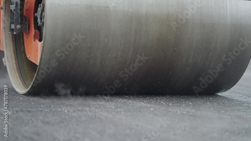 Steamroller compactor cylinder flatten out the new asphalt with steam evaporationg in slow motion. Industrial construction concept photo