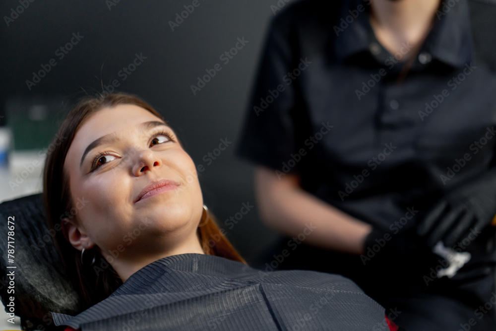 in the dental office a young beautiful girl sits in a chair after the procedure happy and smiling