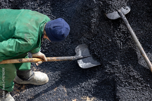 A road service worker scoops up asphalt with a shovel. A worker collects coal with a shovel.