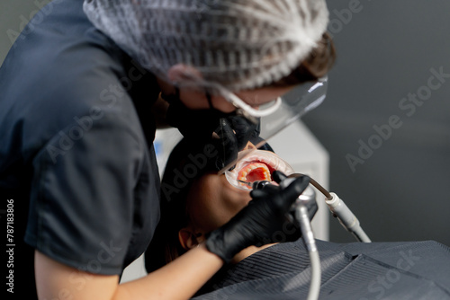 in a dental office female dentist in a cap is routinely cleaning the teeth of a young beautiful girl