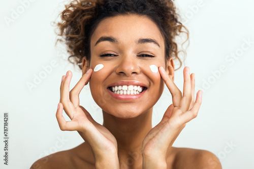 Happy lady applying facial cream on her cheeks