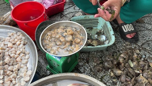 Closeup static shot of an Asian woman's hands while she hastily de-shells prawns with a small knife and sorts the shelled shrimp into different baskets while sitting. on table. photo