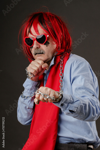 Portrait of a crazy aggressive man in a strange outfit with a metal chain and heart-shaped glasses