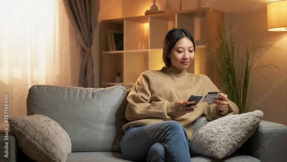 Mobile banking. Online payment. Internet transaction. Relaxed satisfied woman using credit card and phone sitting home room interior. Mobile banking. Online payment. Internet transaction. Relaxed satisfied woman using credit card and phone sitting home room interior.
