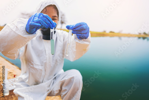 Scientists with protective suit holding a test tube with sample water in her hands. Water pollution examine concept	