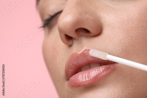 Woman applying lip gloss on pink background  closeup. Space for text
