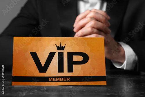 Man sitting at table with VIP sign on grey background, closeup