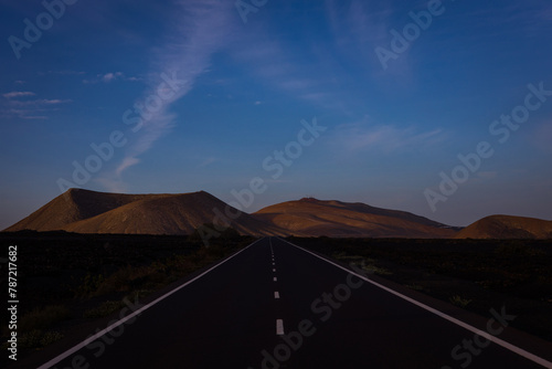 Long empty street between lava fields leading from Yaiza to the volcanic territory of Timanfaya National Park on Lanzarote, Canary Islands. Sunrise Tarmac Road  photo