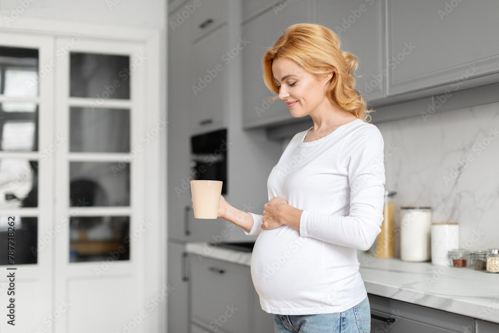 Smiling pregnant woman with a cup in the kitchen Smiling pregnant woman with a cup in the kitchen