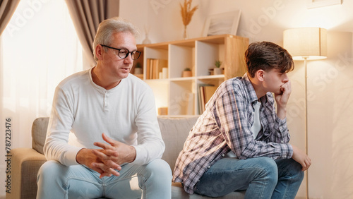 Family misunderstanding. Diverse generation. Relatives quarrel. Offended frustrated dad and son feeling embarrassed after conflict sitting sofa home interior.