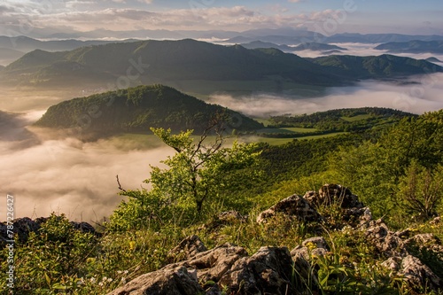 Rocky, forested hill emerges from the valley in the mist. Beautiful morning in the mountain landscape with mists. Morning fog. Sulovske skaly, Velky Manin Povazie photo