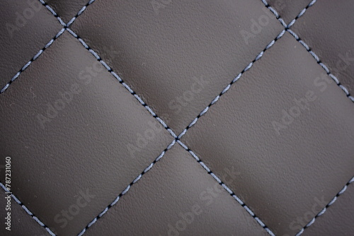 Light blue contrast thread extreme close-up on a dark gray leather car seat