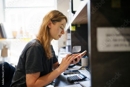 Woman looking at smart phone at desk in office photo