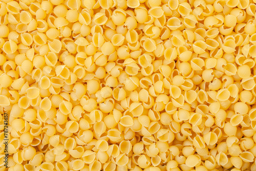 Uncooked, yellow shell pasta background. Top view