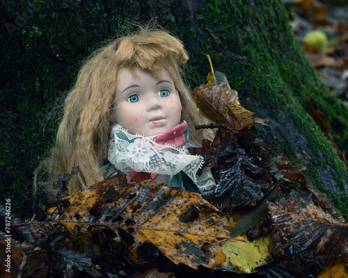 A horror concept. Of a creepy vintage doll, buried under leaves in a spooky autumn forest