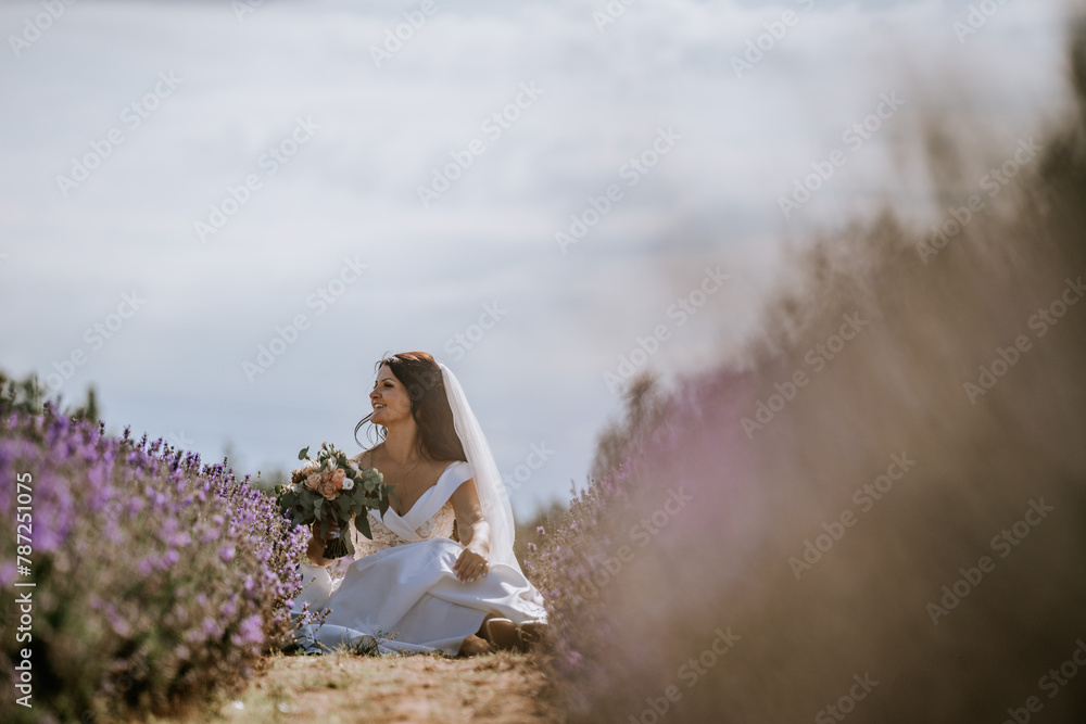 Valmiera, Latvia- July 28, 2024 - A bride sits amidst lavender, gazing away thoughtfully, veiled in soft light with blooms and sky in the backdrop. Valmiera, Latvia- July 28, 2024 - A bride sits amidst lavender, gazing away thoughtfully, veiled in soft light with blooms and sky in the backdrop.