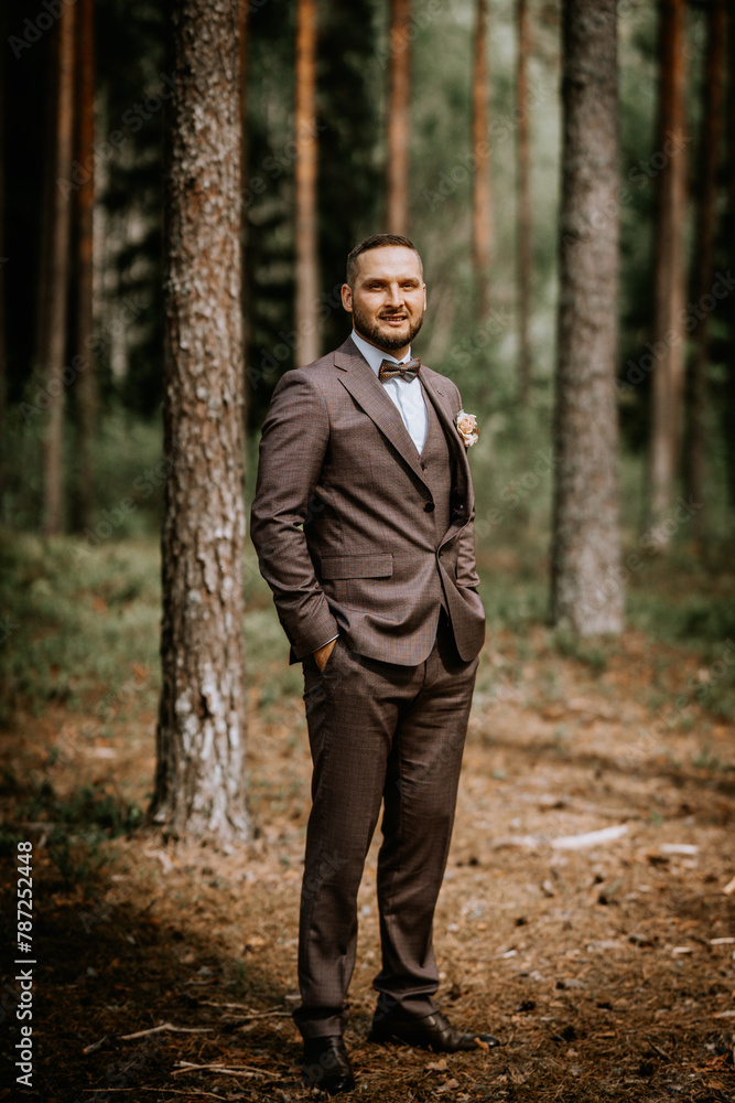 a man standing in a forest. He is dressed in a brown three-piece suit with a white shirt and a patterned bow tie. He appears confident, possibly celebrating a special occasion. a man standing in a forest. He is dressed in a brown three-piece suit with a white shirt and a patterned bow tie. He appears confident, possibly celebrating a special occasion.