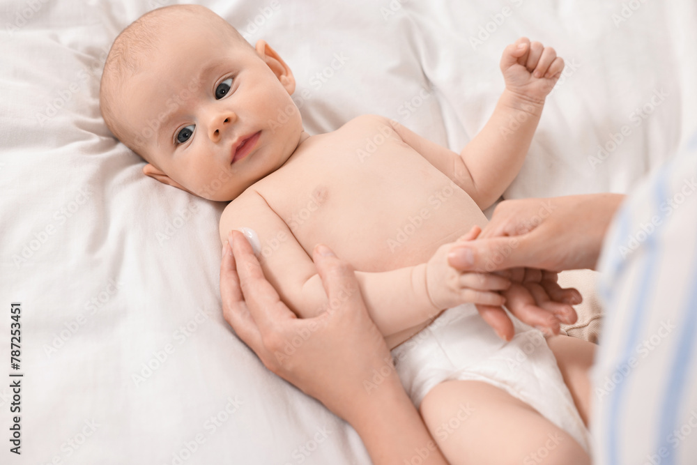 Woman applying body cream onto baby`s skin on bed, above view Woman applying body cream onto baby`s skin on bed, above view