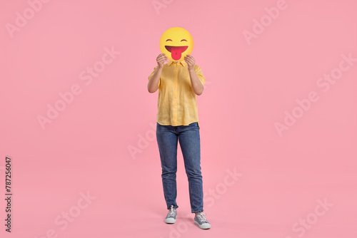 Woman covering face with emoticon sticking out tongue on pink background