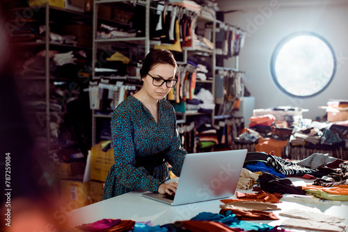 Female fashion designer working on laptop in textile studio with fabric samples