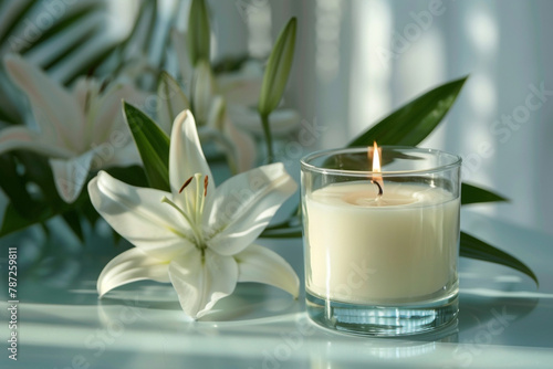 Candle in a transparent glass. Relaxation atmosphere with white lilies decoration. Bokeh background.