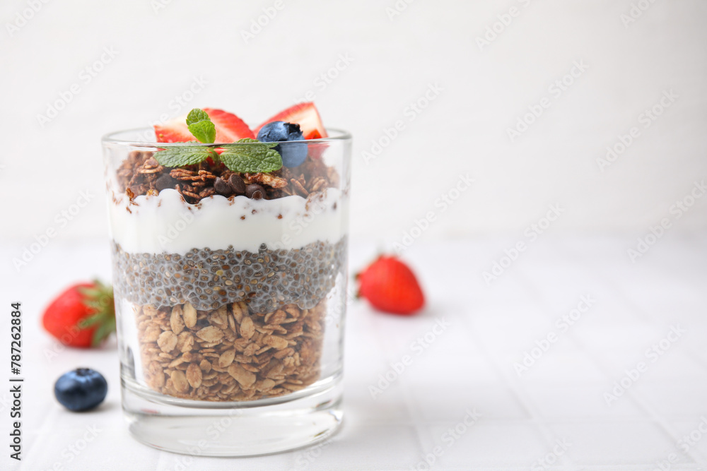 Tasty granola with berries, yogurt and chia seeds in glass on white tiled table, space for text Tasty granola with berries, yogurt and chia seeds in glass on white tiled table, space for text