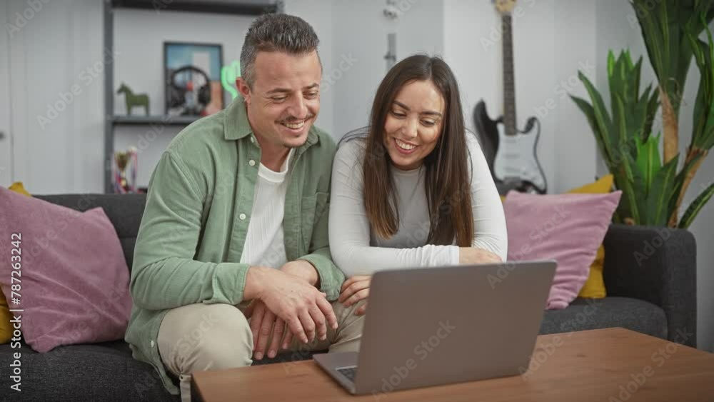 A happy couple enjoys a video call together in a cozy living room, conveying a sense of love, communication, and home comfort. A happy couple enjoys a video call together in a cozy living room, conveying a sense of love, communication, and home comfort.