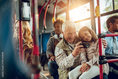 Bilde på lerret Grandfather and granddaughter taking pictures on city bus with passengers