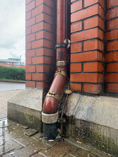 Фотография A brown drainpipe going into the ground against the background of a brown brick wall in Germany, the city of Ludwigsburg