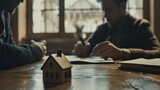 A close view of two people engaging in a real estate transaction with a wooden model house on the table, capturing the concept of property dealing