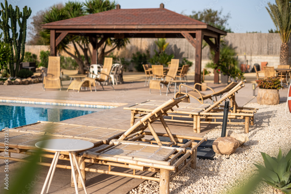 Bamboo sun loungers by a serene pool, inviting for peaceful relaxation, warm, sunny ambiance ideal for leisure retreats.