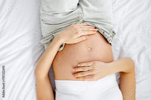 A pregnant woman in jeans with an open stomach strokes him with her hands. The future mother. The expectant mother is waiting and preparing for the birth of a child at home in a bright bedroom