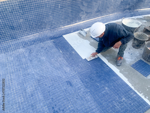 Operario de la construcción pavimentando con gresite azul una piscina en una obra de construcción 
