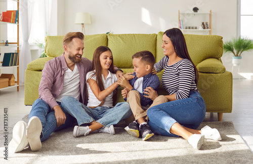 Portrait of happy laughing kids boy and girl having fun with their parents, sitting on the floor at home. Portrait of young couple family spending time together with children. Family leisure concept.