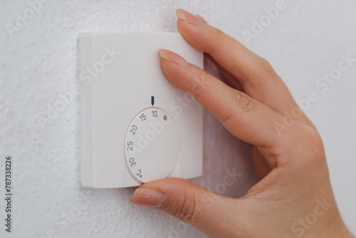 Hand turns down the temperature to 10 degrees Celsius on an electronic thermostat. Symbol for saving energy. An empty house during the holidays