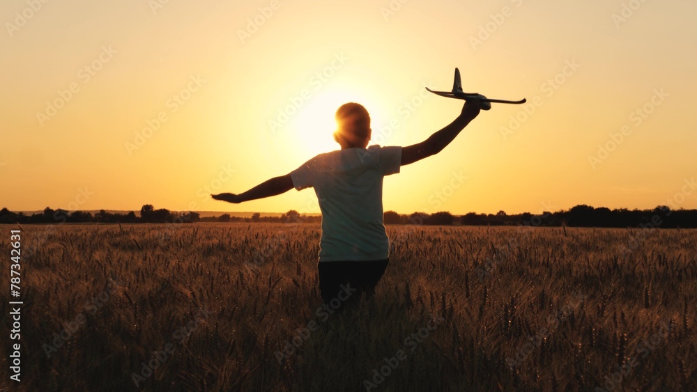Cheerful boy teen running with plane toy on autumn wheat field at cinematic sunset sunrise back view closeup. Active male kid playing flying airplane plaything enjoy freedom happy childhood at meadow - obrazy, fototapety, plakaty 