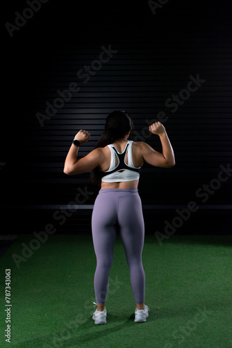young female athlete wearing sportswear from behind raising her arms to show her back