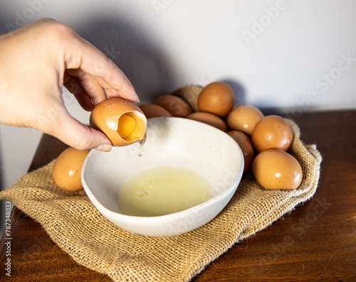 A hand holds a broken egg. Separating the white from the yolk, background with chicken eggs for a recipe