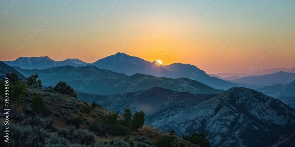 A scenic view of mountains with the partially eclipsed sun rising behind them. 