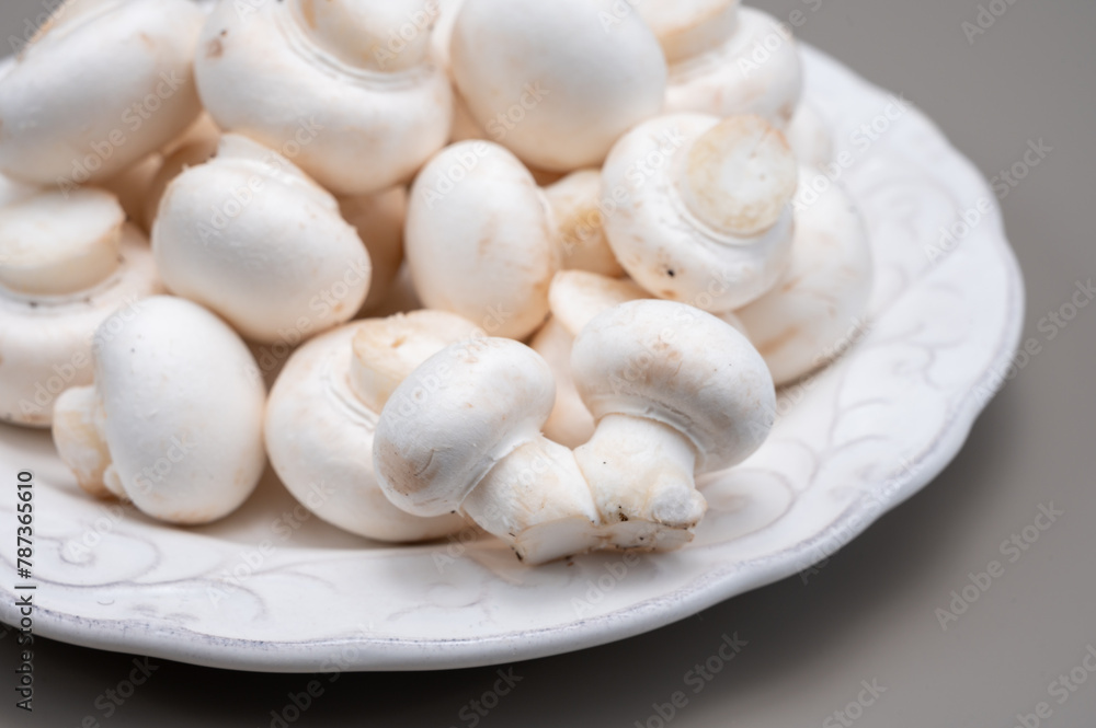 White champignon mushrooms fresh uncooked on white ceramic plate copy space
