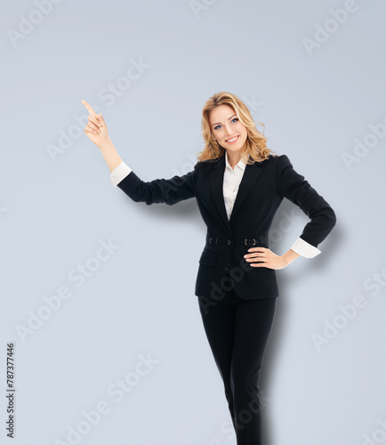 Full body happy, excited confident business woman, businesswoman showing pointing finger up copy space empty slogan text area. Isolated grey gray background. Ad concept image.