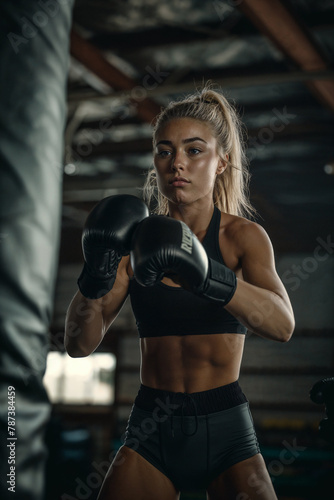 Determined female boxer training with heavy bag. Focused woman in athletic gear practicing punches on a heavy boxing bag in gym