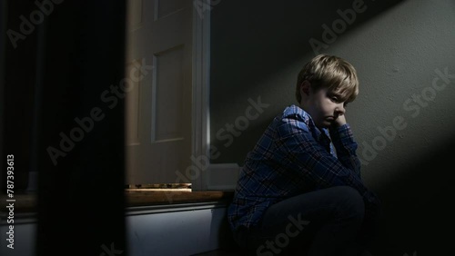 A young boy sadly sits on a dark stair case in a home photo