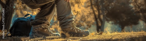 A man in hiking boots is kneeling on the ground next to his backpack in the woods.
