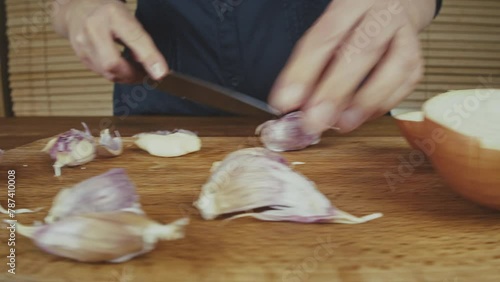Woman's hands close up cutting onion and smashing, and peeling garlic on a wooden board with a big knife. Wooden kitchen table. . High quality 4k footage